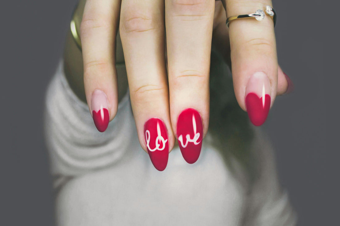 Close-up of hand with elegant red gel nail art spelling 'love,' perfect for showcasing intricate nail designs.