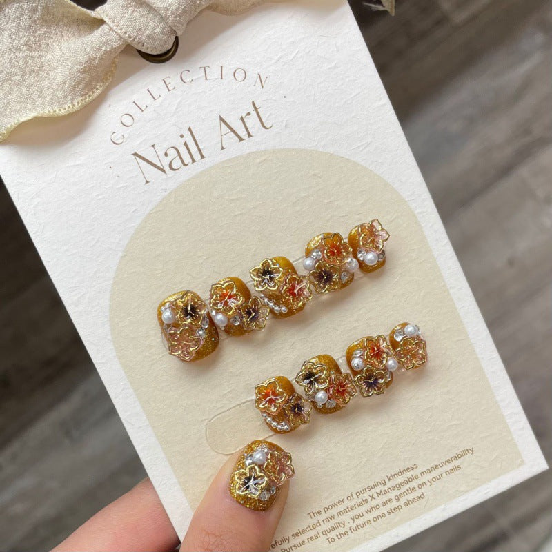 Golden Mayflowers press-on nails displayed on a card, featuring a rich gold base adorned with multicolored floral accents and crystal embellishments for a luxurious look.