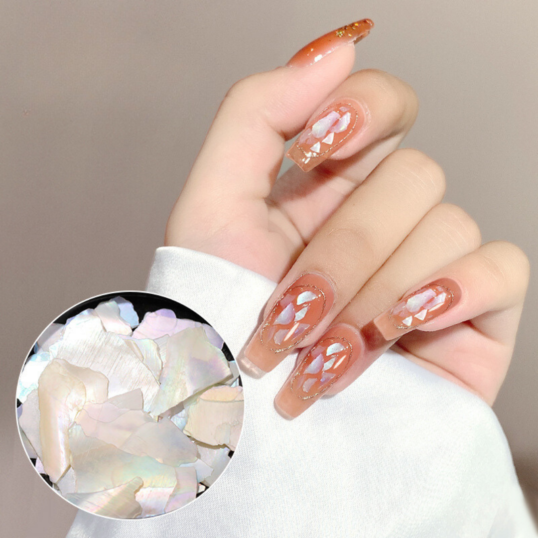 Hand modeling nails decorated with faux oyster shell flakes, displaying a detailed and glossy finish on a set of stiletto nails, enhancing the manicure with a luxurious and reflective touch