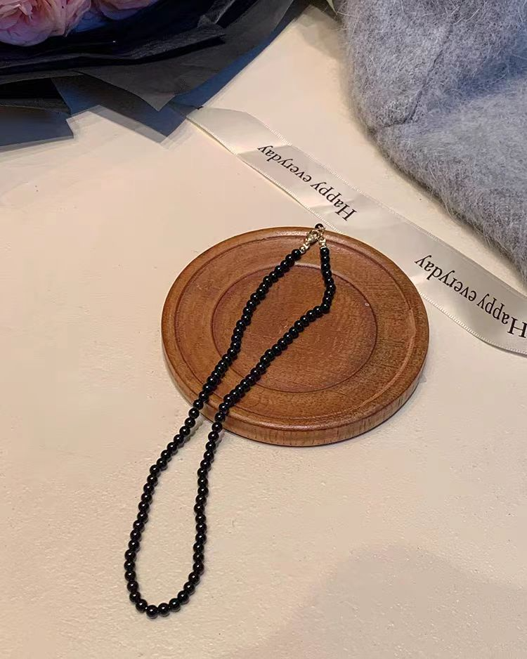 Black pearl-style bead necklace displayed on a round wooden tray