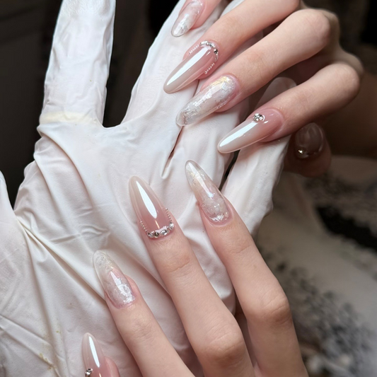 Close-up of glossy nude almond press-on nails with silver flakes and crystal-look accents