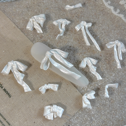 Assorted pearl white resin ribbon bows displayed around a nail tip