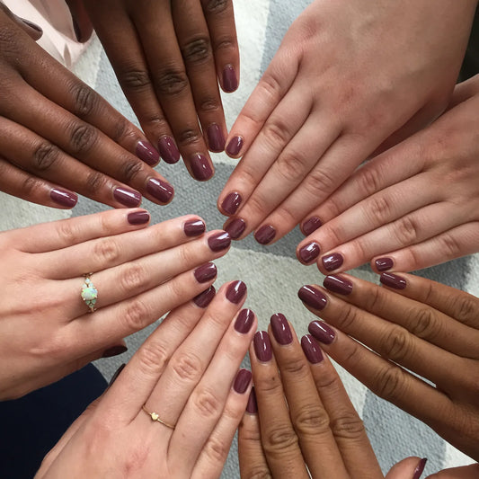 Image of hands of all skin tones with same short square nails with pale maroon nail polish.