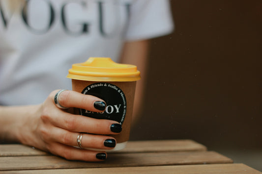 A hand holding a coffee cup, showcasing a chic black gel manicure.