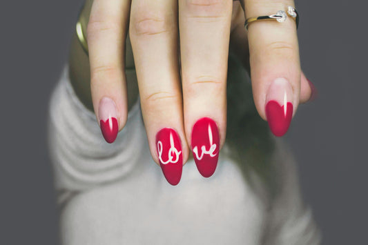 Close-up of hand with elegant red gel nail art spelling 'love,' perfect for showcasing intricate nail designs.