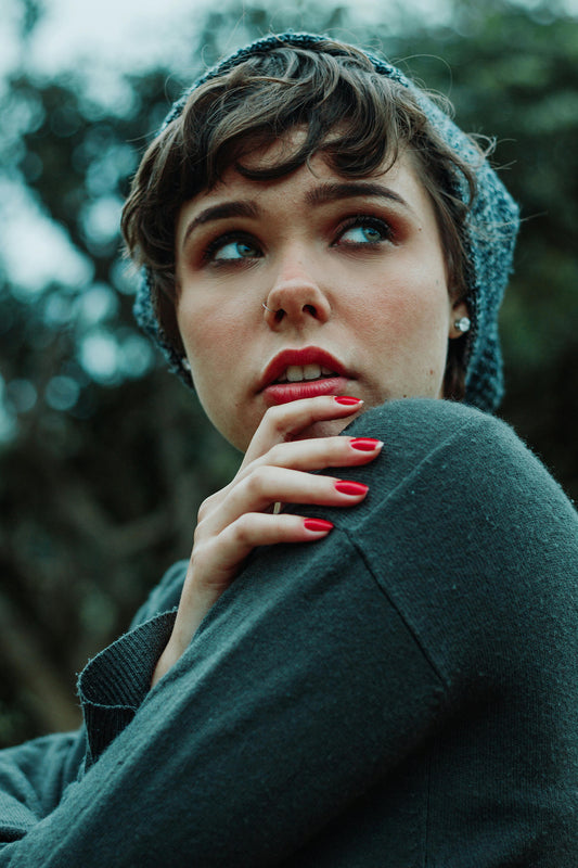 Young woman with short hair, dressed in a winter coat, displaying her nails painted with a dark red nail polish.