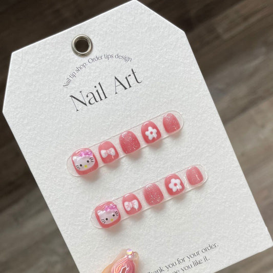 Hello Kitty - Pink press-on nails on a card, featuring a vibrant pink color palette with detailed Hello Kitty figures and floral appliqués for a cute and girlish manicure.