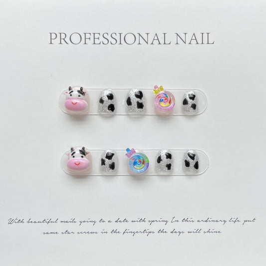 Adorable 'MINI MOO' press-on nails featuring playful cow print and cute 3D embellishments like a pink cow face and colorful candy, perfect for fun and creative nail art.