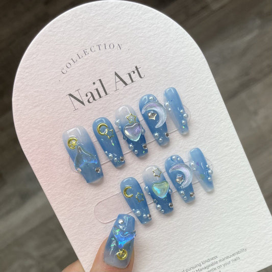 Set of blue moon-themed press-on nails featuring a dreamy sky blue base adorned with golden crescent moons, glitter, and iridescent heart charms. These nails are perfect for creating a celestial-inspired look, combining elegance with whimsy.