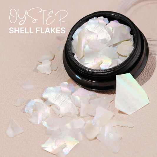 Open container of faux oyster shell flakes spread out on a surface, showing their iridescent and reflective properties, ideal for adding a shimmering effect to nail art designs