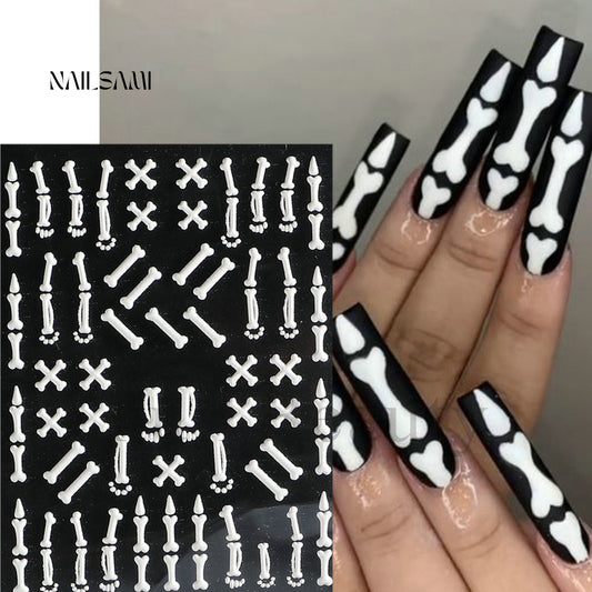 "Bones & X's - Skeleton" nail stickers by NAILSAMI feature various white skeletal designs such as bones and skulls on a black sheet, applied to nails for a dramatic monochrome effect.