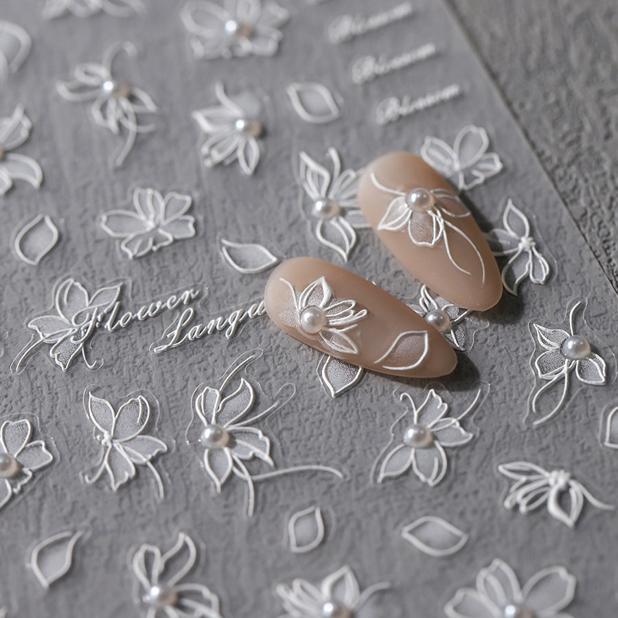 Elegant white floral nail stickers with delicate pearl accents arranged on a gray background. Two nude-colored nails are decorated with the floral stickers, creating a sophisticated and intricate design.