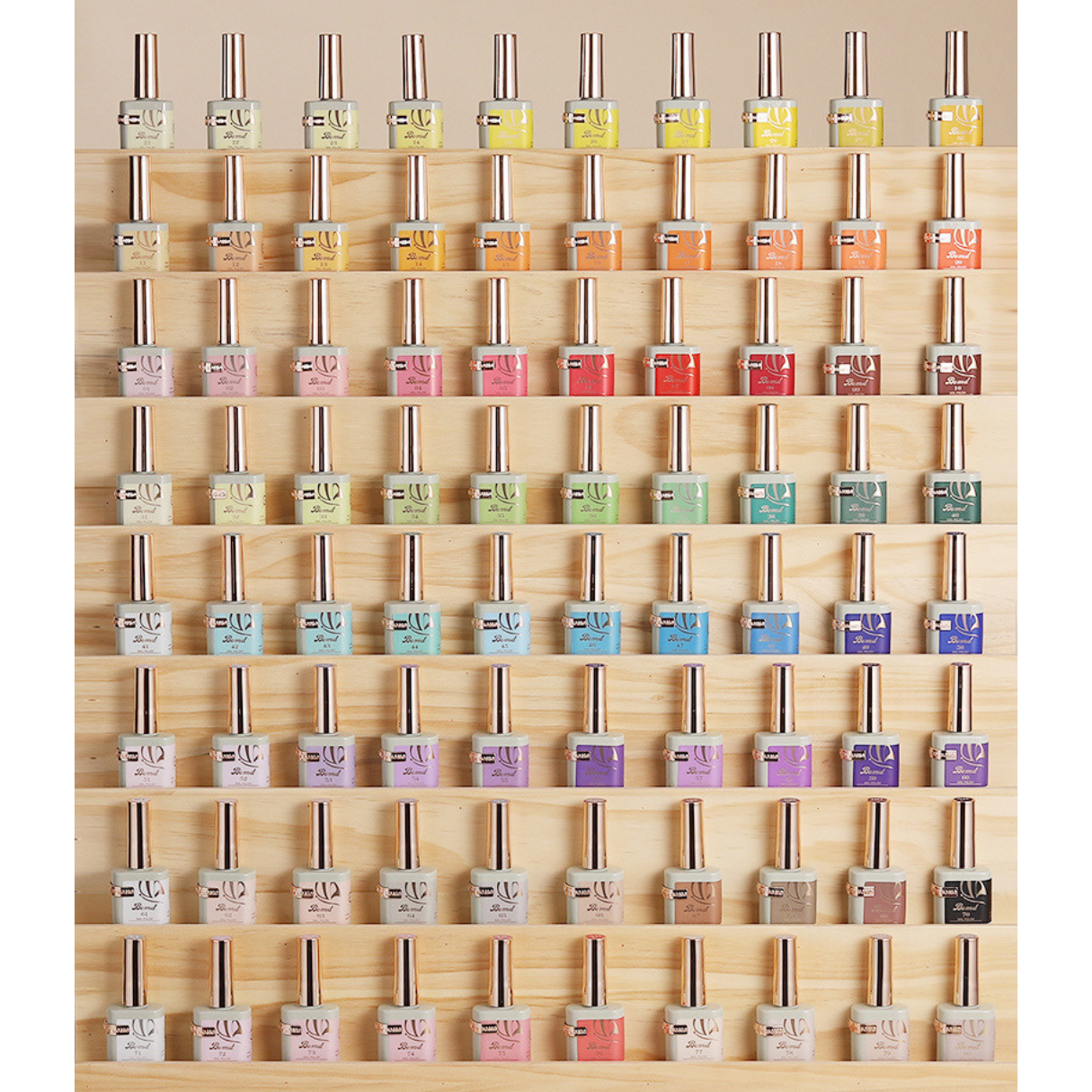 A neatly organized display of BOMD gel polish bottles, arranged by color on a wooden shelf. The collection showcases a wide spectrum of shades, from warm oranges and reds at the top to cool blues and purples at the bottom, reflecting the extensive variety offered by the brand.