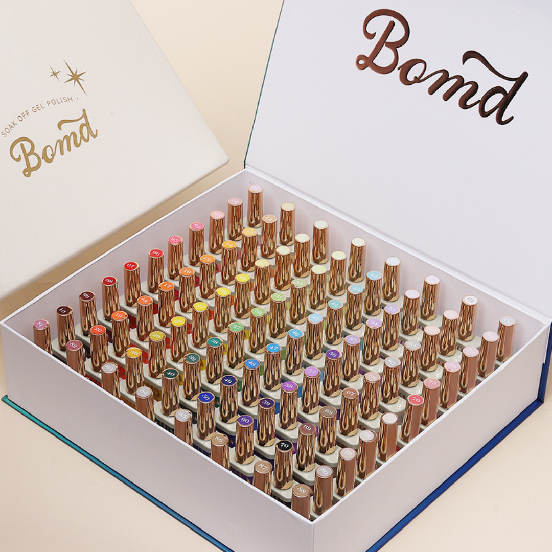 Open box displaying a full set of 88 colorful gel polishes with gold caps, neatly arranged in rows. The kit includes prep gels and is paired with a UV/LED nail lamp, all branded under 'BOMD.' The image showcases the complete collection, highlighting the variety of colors available in the kit.