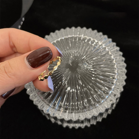Gold-tone wavy metal adjustable ring held above a glass dish