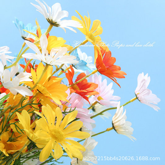 Mixed-colour artificial daisy flower sprays against a blue photography backdrop