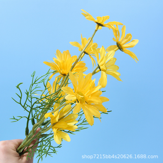 Yellow artificial daisy flower spray held against a blue background