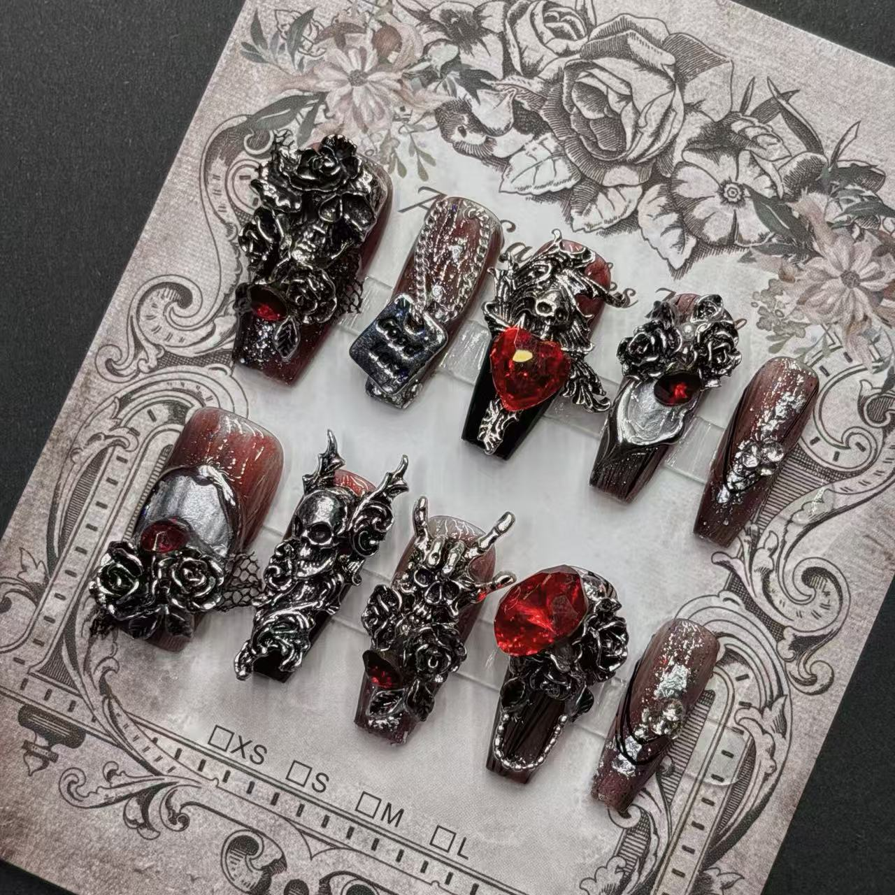 Angled view of burgundy 3D gothic press-on nails with skulls and red gem-like accents