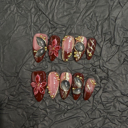 Burgundy floral cat-eye almond press-on nails with nude pink and gold-tone accents