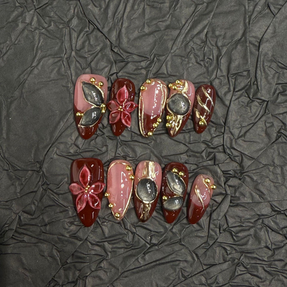 Burgundy almond press-on nail design with raised red flowers and metallic-look accents