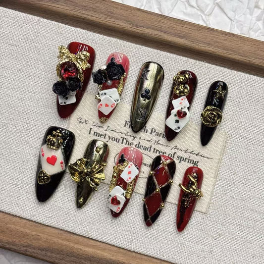 Long pointed burgundy playing-card press-on nails with black roses and gold-tone details
