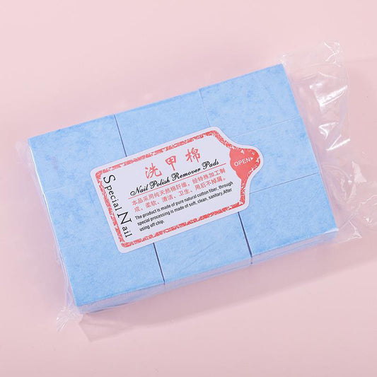 A package of nail polish remover pads, neatly arranged in a clear plastic wrapper. The pads are light blue in color and made of a soft, absorbent material. The packaging features a label with red and white design elements, displaying the text "Nail Polish Remover Pads" along with product information in both English and Chinese. The label emphasizes the use of pure natural cotton fiber, ensuring a clean and sanitary nail polish removal process.