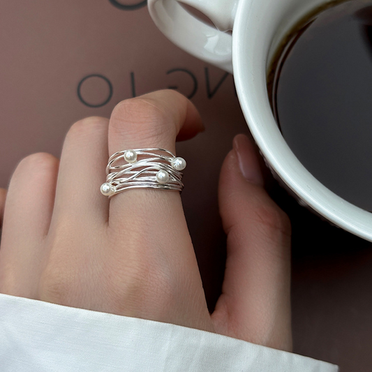 Irregular multi-layer pearl open ring worn on a hand beside a coffee cup