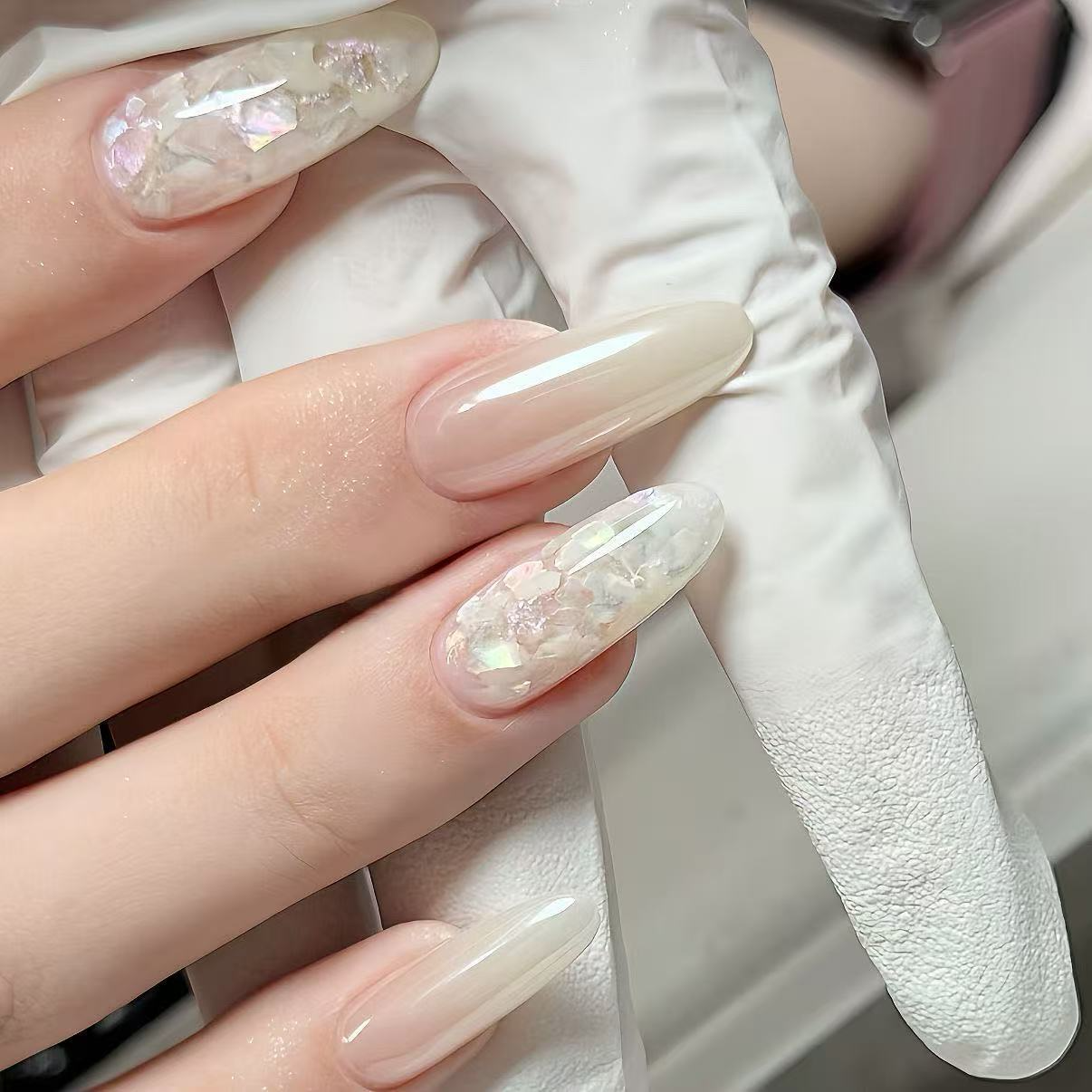 Close-up of glossy nude pink oval press-on nails with iridescent shell flakes
