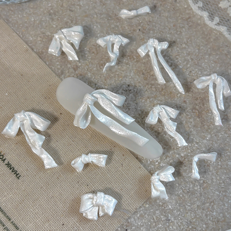 Assorted pearl white resin ribbon bows displayed around a nail tip