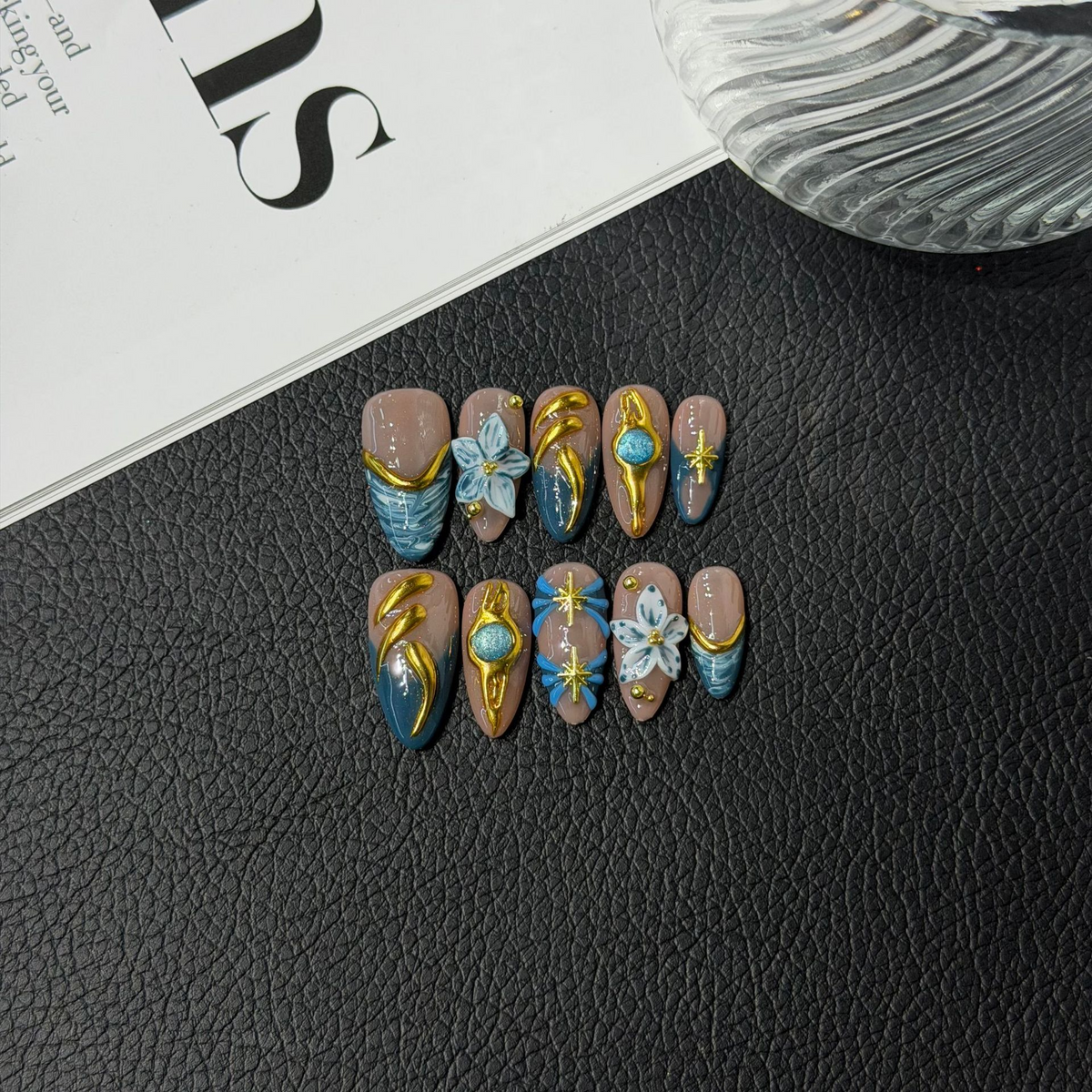 Teal floral almond press-on nails with translucent nude and sculptural gold-tone accents