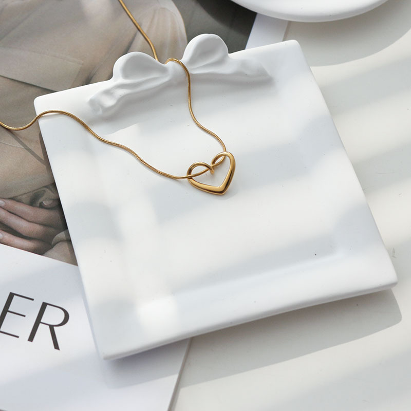 Square white plaster tray with a sculpted bow and heart pendant necklace