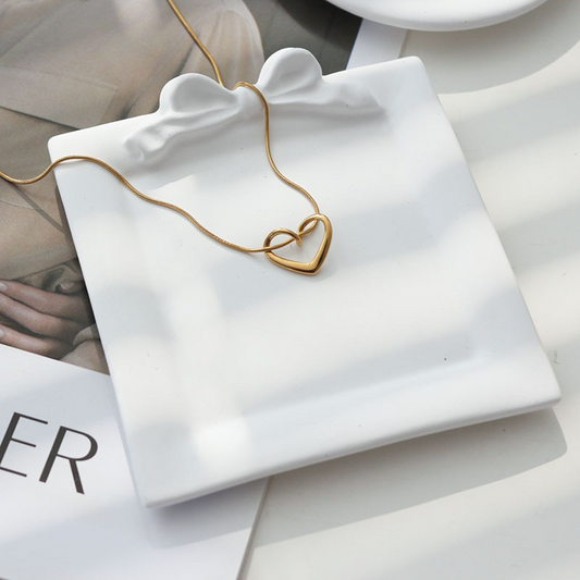 Square white plaster tray with a sculpted bow and heart pendant necklace